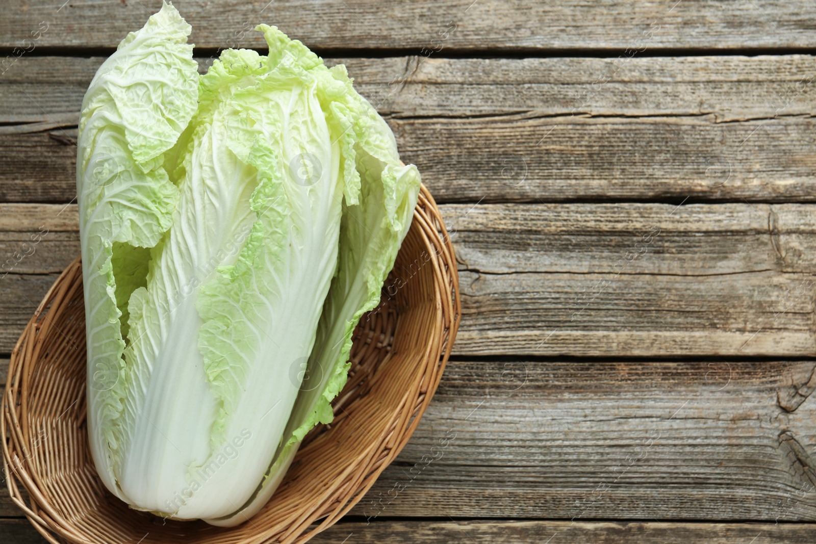 Fresh Chinese cabbage in wicker basket on wooden table, top view. Space for text Photo of Fresh Chinese cabbage in wicker basket on wooden table, top view. Space for text