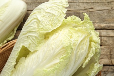 Photo of Fresh Chinese cabbages in wicker basket on wooden table, top view