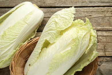 Photo of Fresh Chinese cabbages in wicker basket on wooden table, top view
