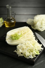 Photo of Cut Chinese cabbage and knife on black table, closeup
