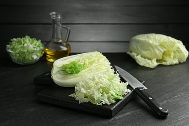 Photo of Cut Chinese cabbage and knife on black table, closeup