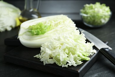 Photo of Cut Chinese cabbage and knife on black table, closeup