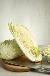 Photo of Fresh Chinese cabbages and knife on light grey table, closeup
