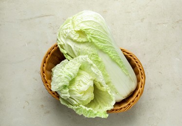 Photo of Fresh Chinese cabbages in wicker basket on light grey table, top view
