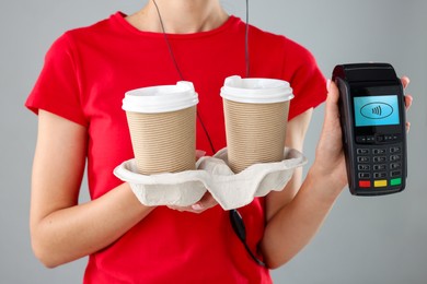 Image of Worker holding payment terminal and takeaway cups with hot drinks on grey background, closeup