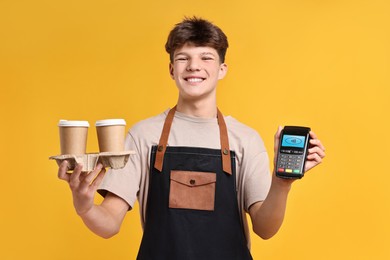Image of Worker holding payment terminal and takeaway cups with hot drinks on orange background
