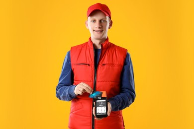 Image of Worker holding payment terminal and credit card on orange background