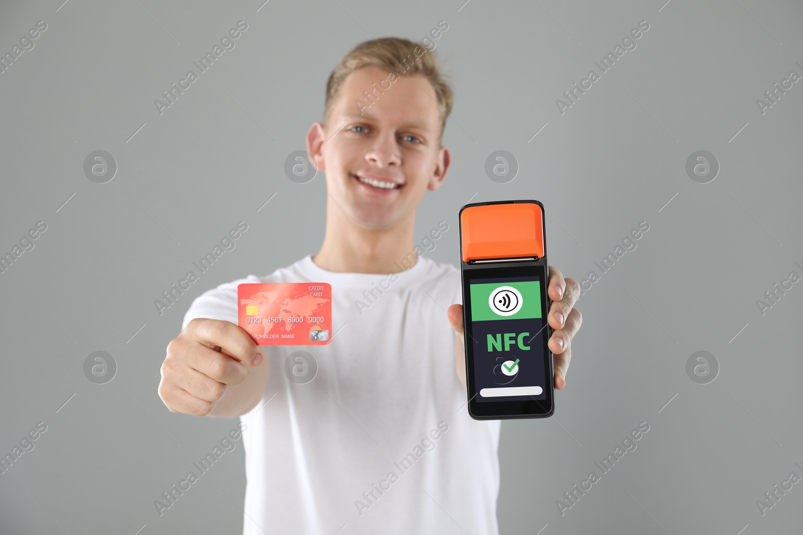 Man holding payment terminal with NFC system and credit card on grey background Image of Man holding payment terminal with NFC system and credit card on grey background