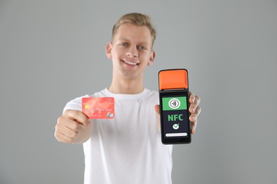 Image of Man holding payment terminal with NFC system and credit card on grey background
