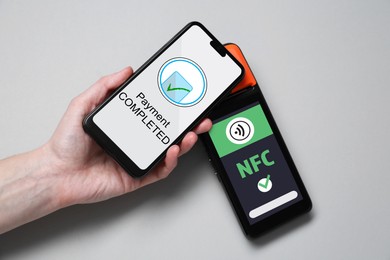 Image of Woman using mobile phone to pay via terminal with NFC system on grey background, top view