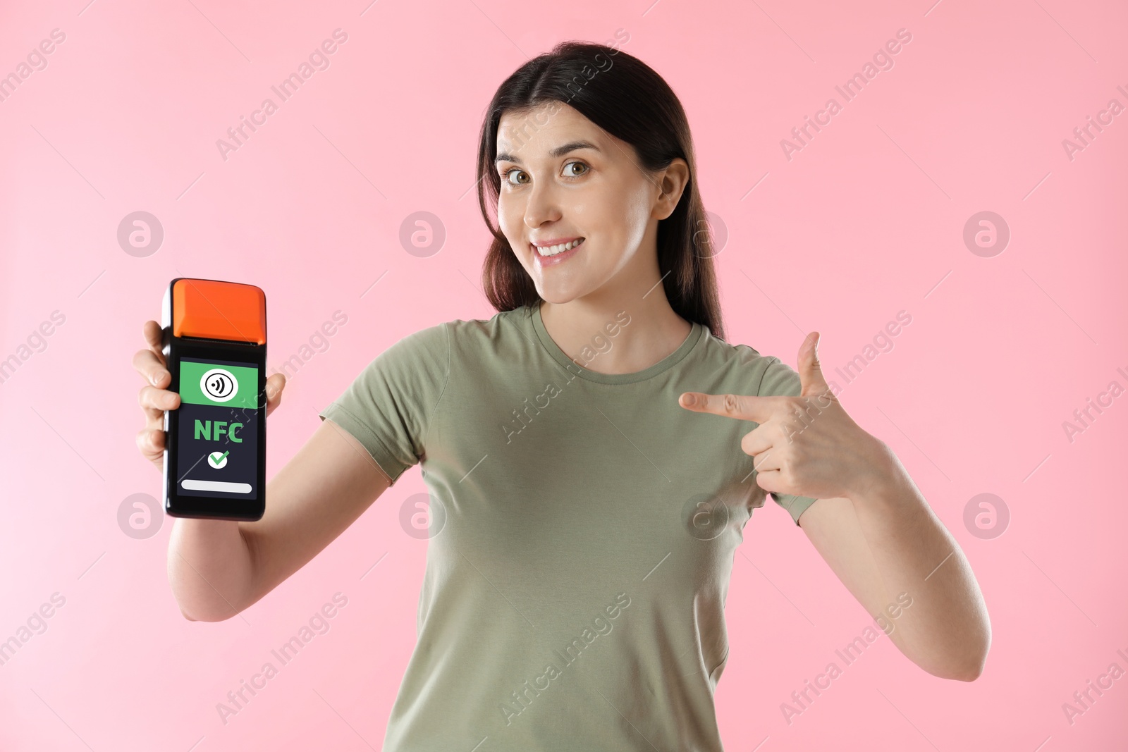 Woman pointing at payment terminal with NFC system in her hand on pink background Image of Woman pointing at payment terminal with NFC system in her hand on pink background