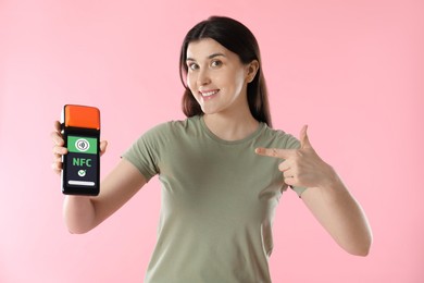 Image of Woman pointing at payment terminal with NFC system in her hand on pink background