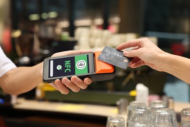 Image of Payment terminal with NFC system. Client using credit card to pay for service in cafe, closeup