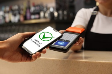 Image of Payment terminal with NFC system. Client using mobile phone to pay for service in bar, closeup