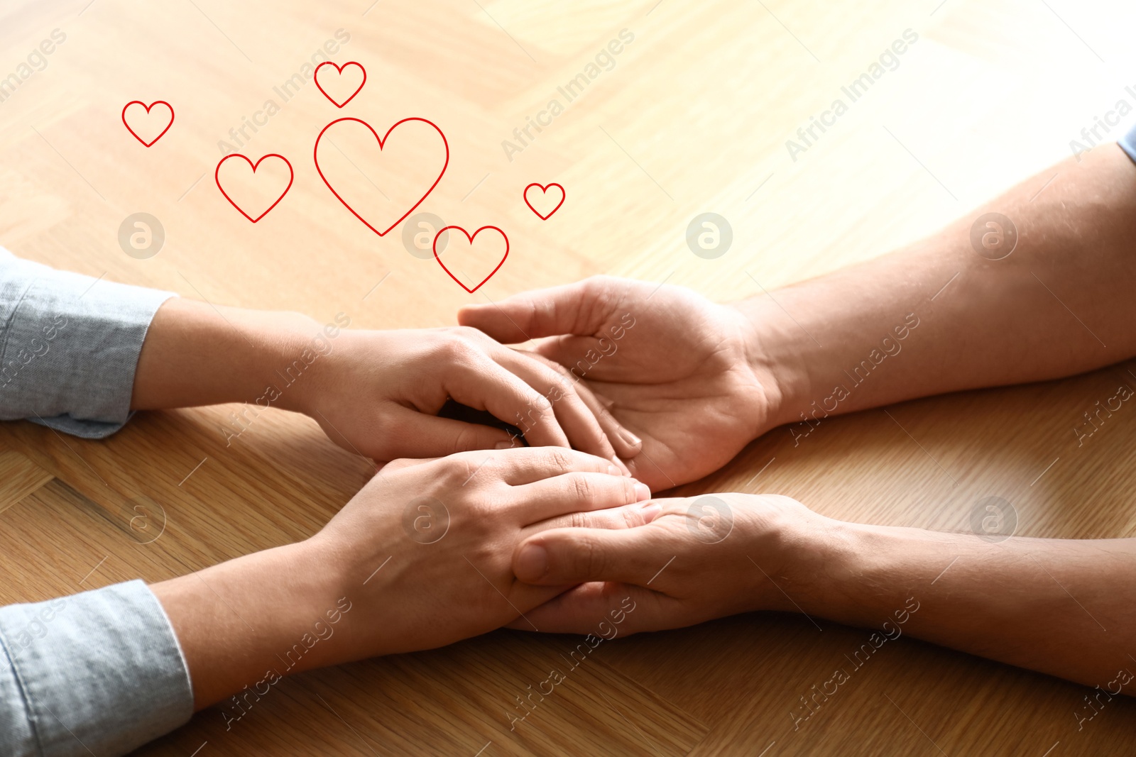 Man and woman holding hands at wooden table, closeup. Drawn hearts near them Image of Man and woman holding hands at wooden table, closeup. Drawn hearts near them