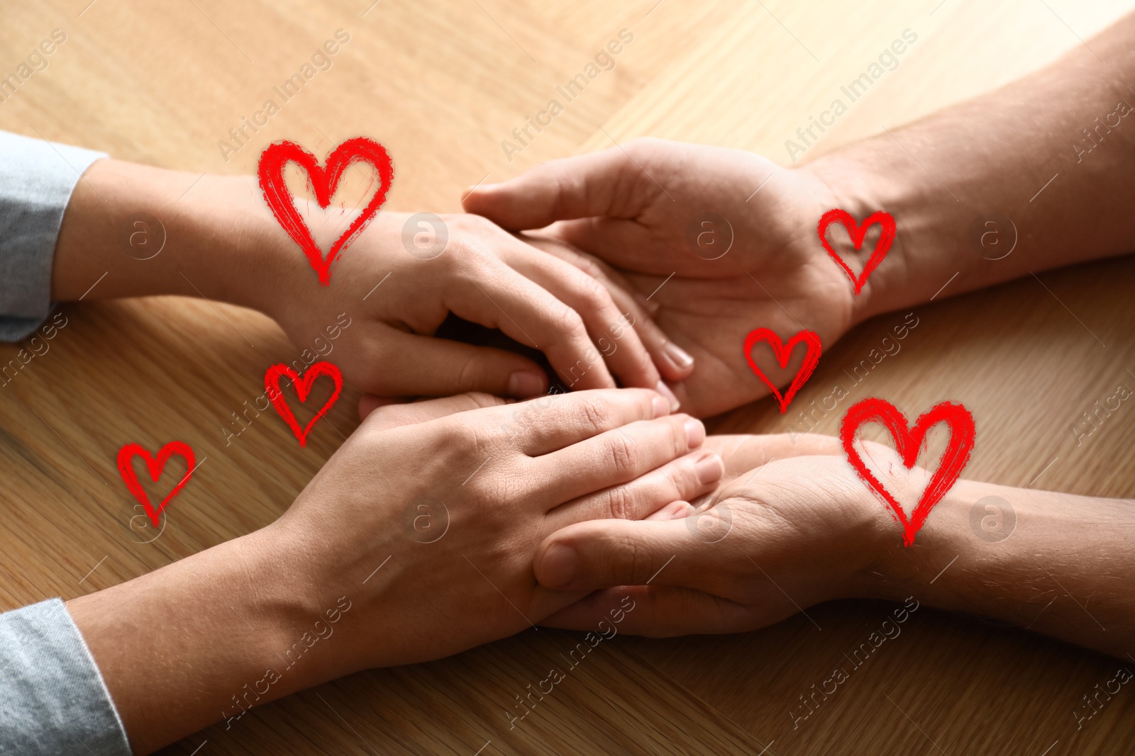 Man and woman holding hands at wooden table, closeup. Drawn hearts near them Image of Man and woman holding hands at wooden table, closeup. Drawn hearts near them
