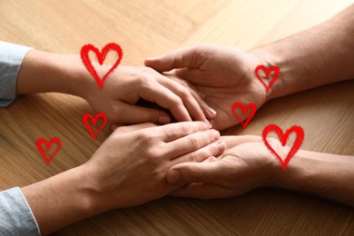 Image of Man and woman holding hands at wooden table, closeup. Drawn hearts near them