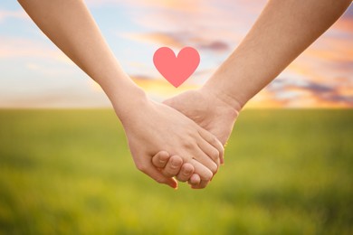 Image of Lovely couple holding hands in green field, closeup. Drawn heart near them