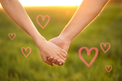 Image of Lovely couple holding hands in green field, closeup. Drawn hearts near them