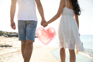 Image of Lovely couple holding hands and walking on beach, closeup. Drawn heart near them