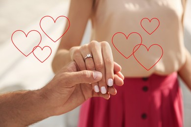 Image of Lovely engaged couple holding hands outdoors, closeup. Drawn hearts near them