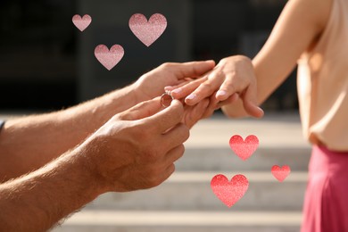 Image of Man putting engagement ring on his girlfriend's finger outdoors, closeup. Drawn hearts near them