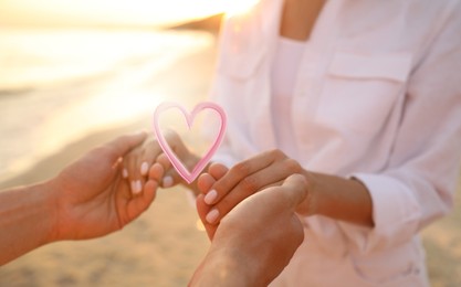 Image of Lovely couple holding hands on beach, closeup. Drawn heart near them