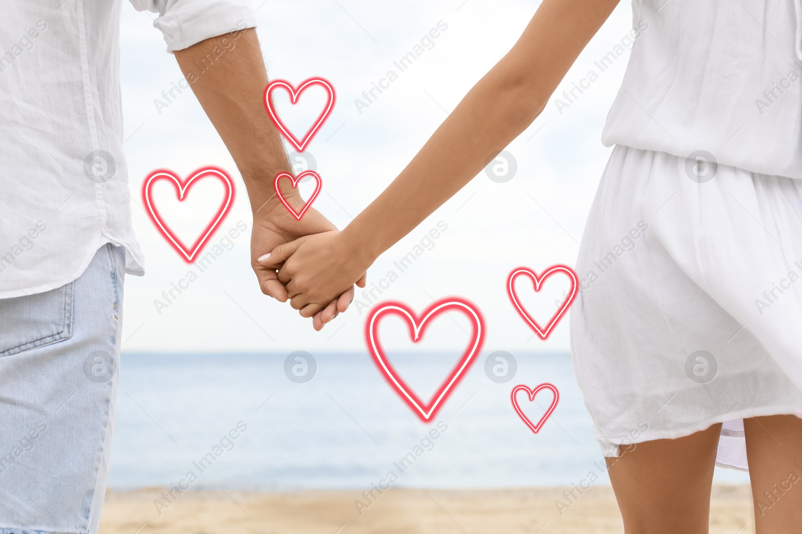 Lovely couple holding hands on beach, closeup. Drawn hearts near them Image of Lovely couple holding hands on beach, closeup. Drawn hearts near them