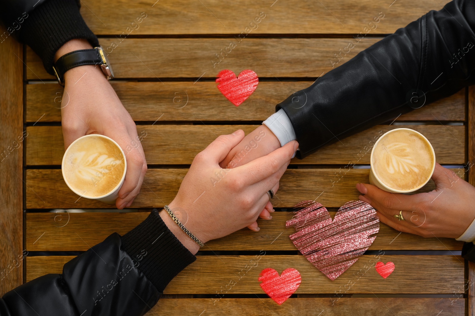 Lovely couple holding hands while drinking coffee at wooden table, top view. Drawn hearts near them Image of Lovely couple holding hands while drinking coffee at wooden table, top view. Drawn hearts near them