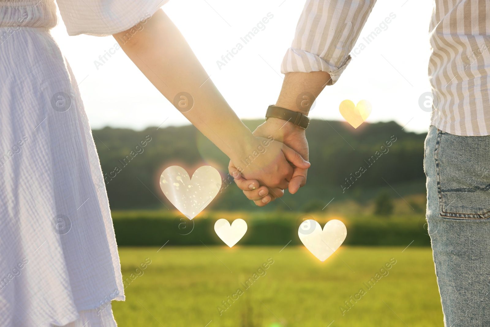 Lovely couple holding hands in green field, closeup. Drawn hearts near them Image of Lovely couple holding hands in green field, closeup. Drawn hearts near them