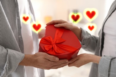 Image of Lovely couple with gift box indoors, closeup. Drawn hearts near them