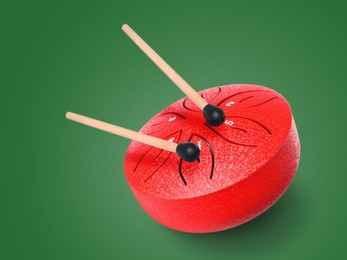Image of Red toy tongue drum in air on green background. Child's musical instrument