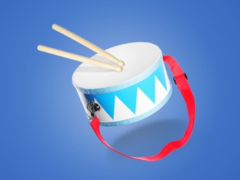 Image of Toy drum and sticks in air on blue background. Child's musical instrument