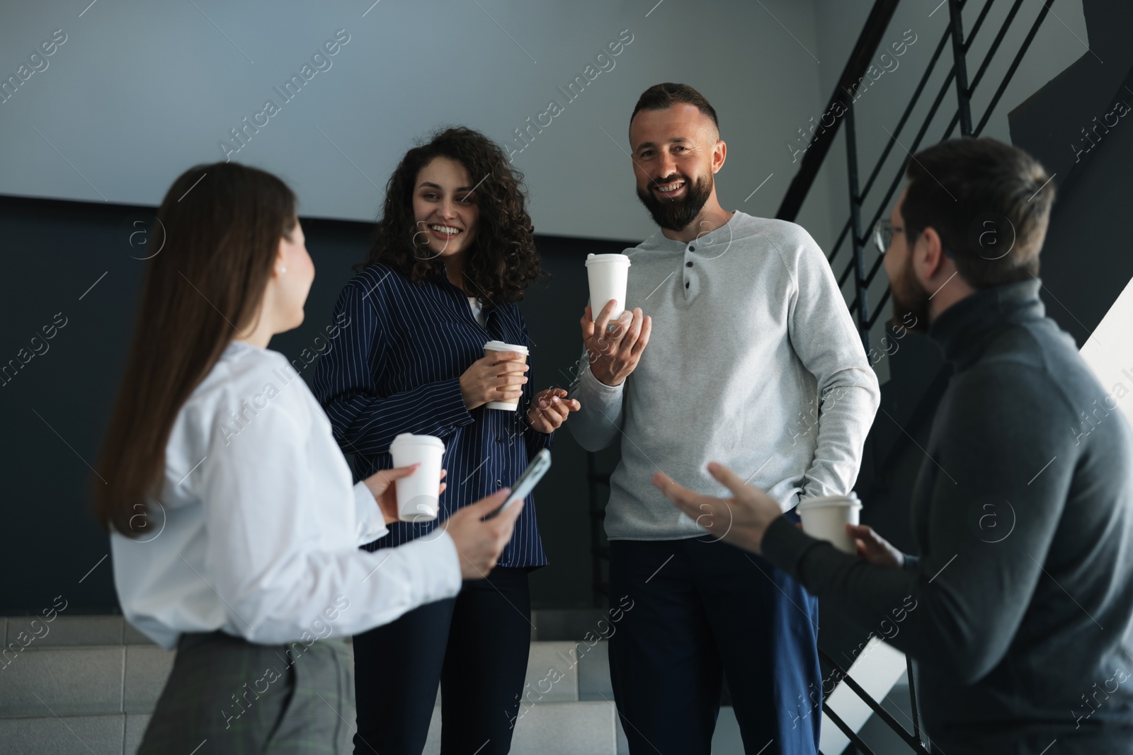 Colleagues with coffee on stairs in office during break Photo of Colleagues with coffee on stairs in office during break