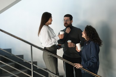 Photo of Colleagues with coffee on stairs in office during break