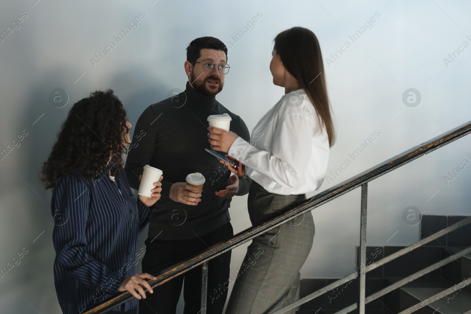Colleagues with coffee on stairs in office during break Photo of Colleagues with coffee on stairs in office during break