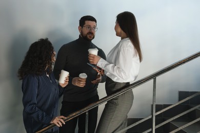 Photo of Colleagues with coffee on stairs in office during break
