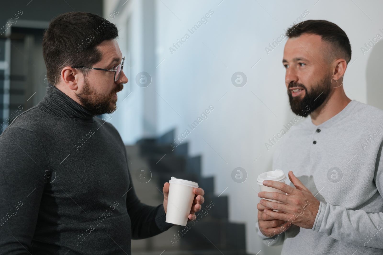 Colleagues with coffee on stairs in office during break Photo of Colleagues with coffee on stairs in office during break