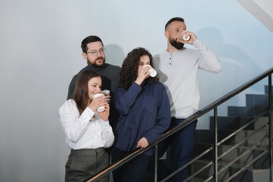 Photo of Colleagues with coffee on stairs in office during break