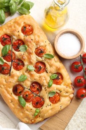 Photo of Delicious focaccia with tomatoes, spices and oil on beige table, flat lay