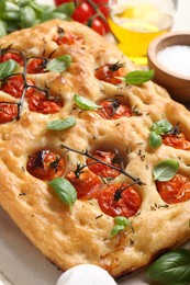 Photo of Delicious focaccia with tomatoes, spices and oil on table, closeup