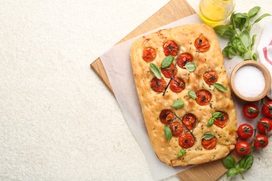 Photo of Delicious focaccia with tomatoes, spices and oil on beige textured table, flat lay. Space for text