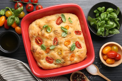 Photo of Delicious focaccia with tomatoes, spices and oil on black wooden table, flat lay