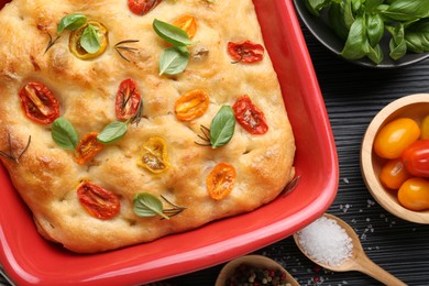 Photo of Delicious focaccia with tomatoes and spices in baking dish on table, flat lay
