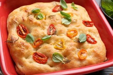 Photo of Delicious focaccia with tomatoes and spices in baking dish on table, closeup