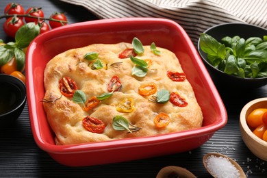 Photo of Delicious focaccia with tomatoes and spices in baking dish on table, closeup