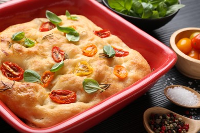 Photo of Delicious focaccia with tomatoes and spices in baking dish on table, closeup