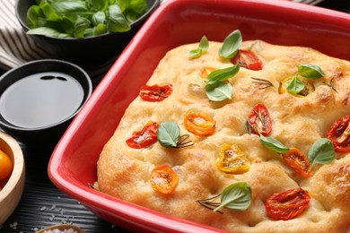 Photo of Delicious focaccia with tomatoes and spices in baking dish on table, closeup