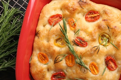 Photo of Delicious focaccia with tomatoes and rosemary in baking dish on table, top view