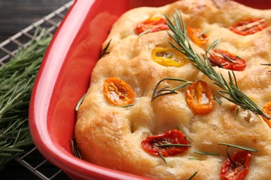Photo of Delicious focaccia with tomatoes and rosemary in baking dish on table, closeup